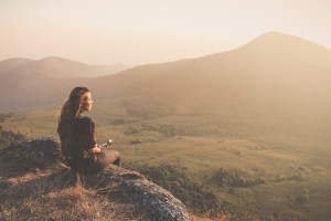 Hipster young girl with backpack enjoying sunset on peak of fogg